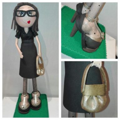 Muñeca artesanal con gafas, vestido negro y bolso dorado. Lleva zapatos altos.