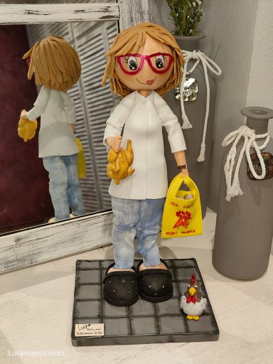 Fofucha personalizada con gafas rojas, sosteniendo un pollo y una bolsa amarilla, y un pollo en el suelo