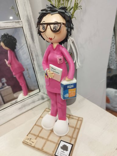 Fofucha personalizada, mujer de pelo corto y gafas, vestida con uniforme rosa de la residéncia y con un paquete de pañales en la mano