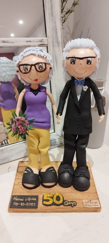 Fofuchas personalizadas, celebrando 50 años juntos, ella con pantalones ocre y jersey lila con ramo en la mano, el traje negro con pajarita
