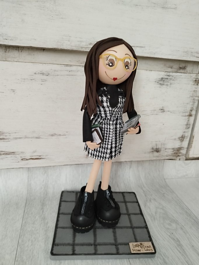 Muñeca  con pelo largo, gafas, vestido a cuadros y botas negras, sobre una base.