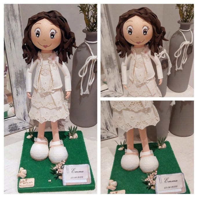 Muñeca con vestido blanco y chaqueta, sonriente, sobre una base decorativa.