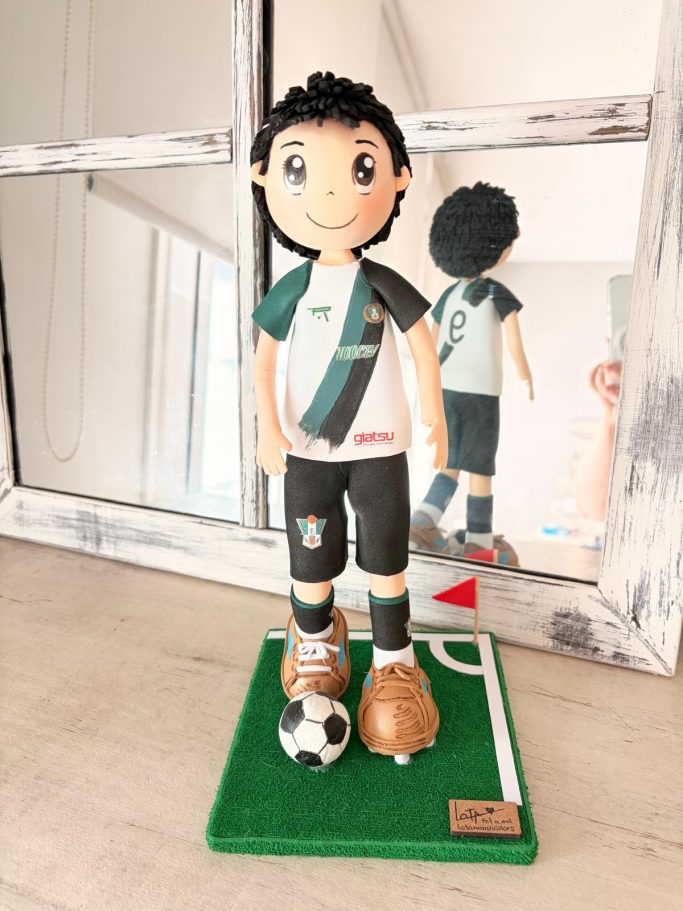 Figura de un niño futbolista con balón, uniforme y base de césped. 