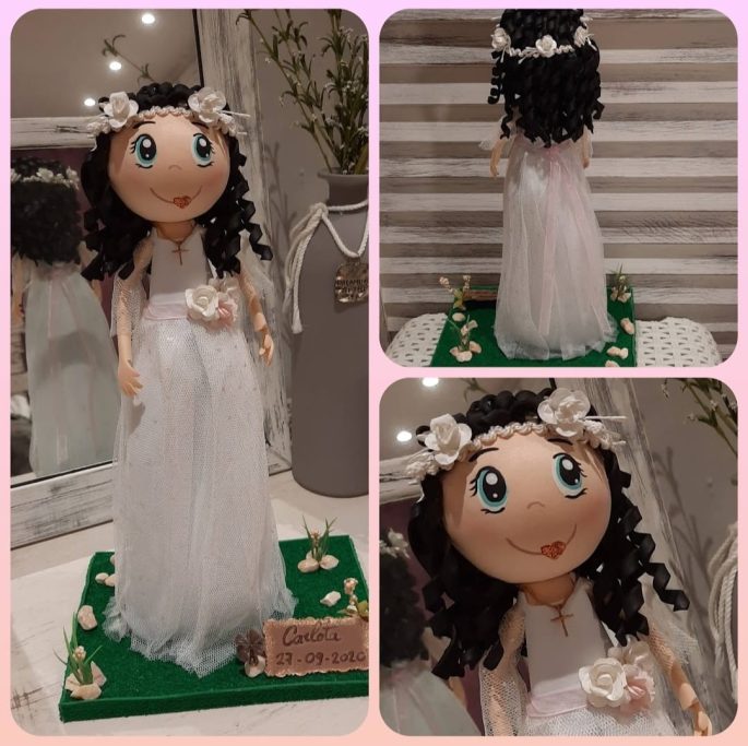 Muñeca con vestido blanco y cabello rizado, adornada con flores en la cabeza.