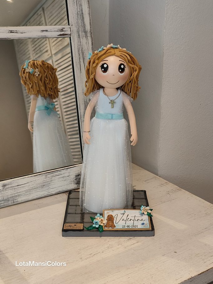 Muñeca con vestido blanco de tul y cabello rizado,con una diadema de flores y cinturón azul claro.