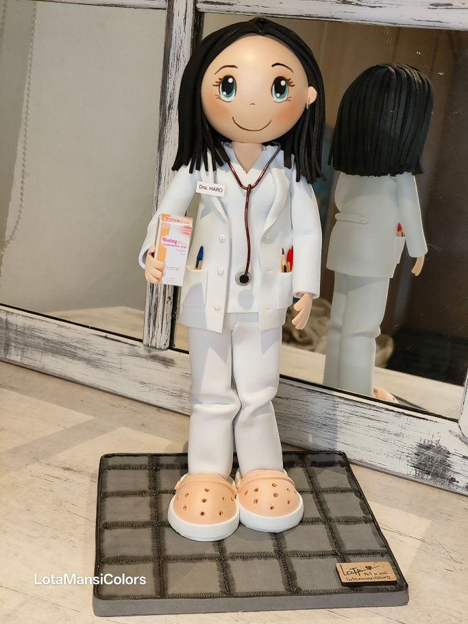 Muñeca con pelo oscuro, vestida de médico, con un fonendoscopio y Dalsy en la mano