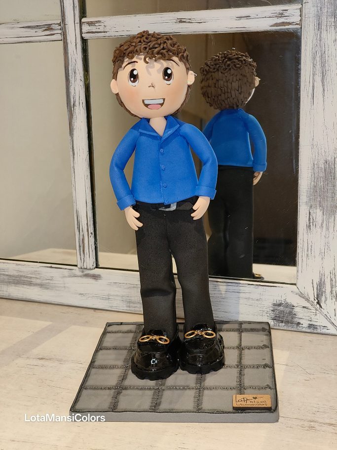 Figura de un niño con camisa azul y pantalones negros, de pie con zapatos de charol en una base cuadrada.