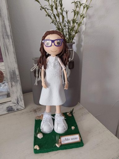 Muñeca con gafas, vestida de blanco de comunión, sobre una base