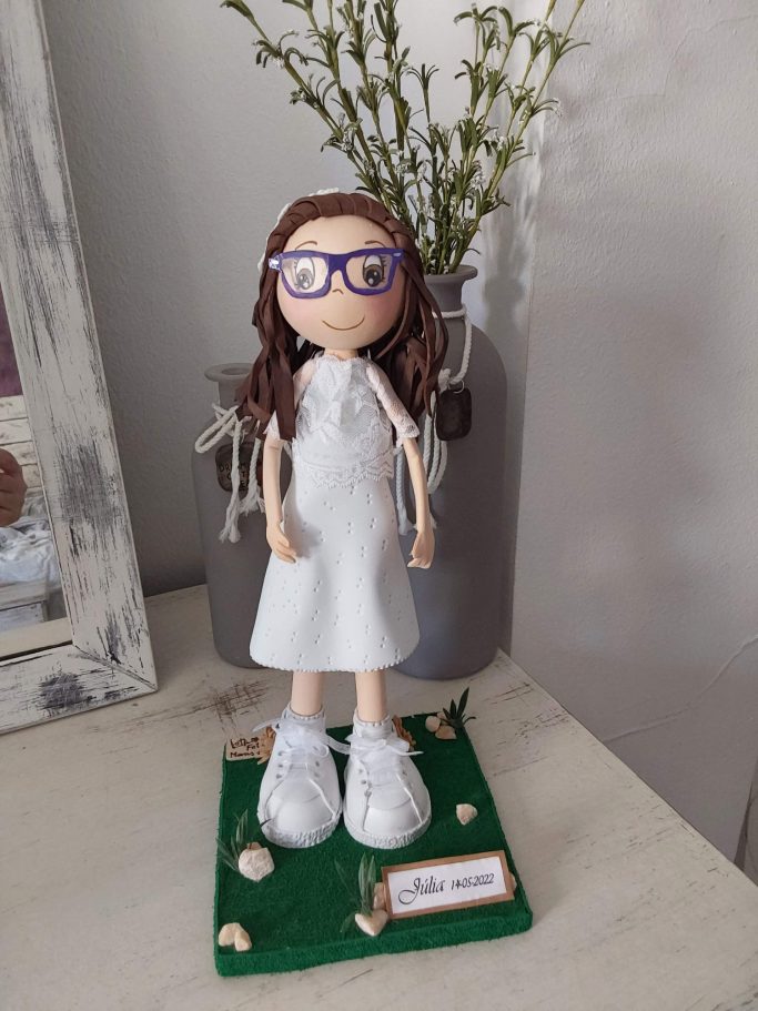 Muñeca  con gafas, vestida de blanco de comunión, sobre una base
