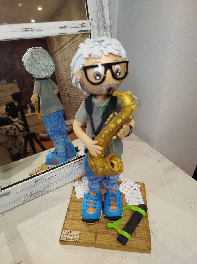 Muñeco con gafas tocando un saxofón, con detalles coloridos y unas partituras en el suelo