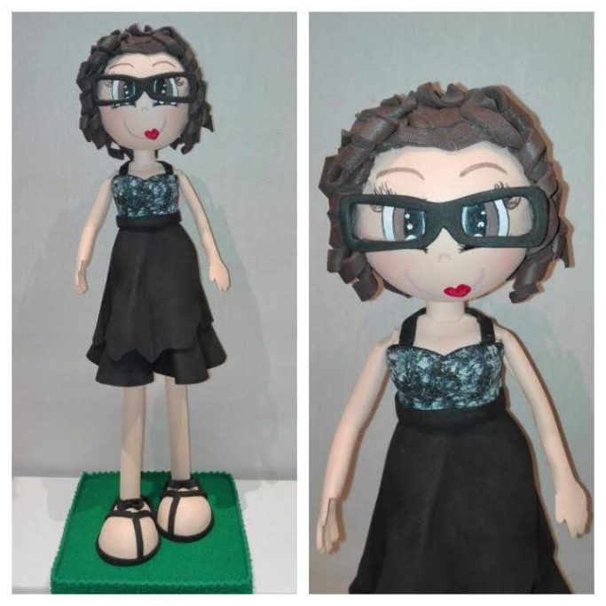 Figurita de goma  eva con vestido negro, gafas y cabello rizado. Base verde.