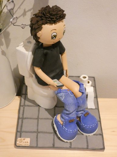fofucha personalizada, sentado en un inodoro,  pantalones bajados, zapatillas azules y leyendo WhatsApp i rollos de papel de wc en el suelo