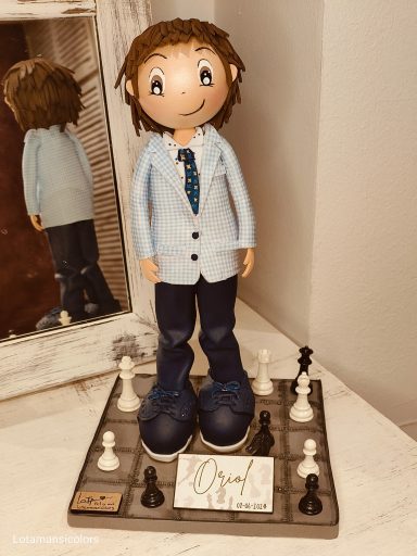 Fofucha personalizada niño de comunión pantalón marino y americana a cuadros azul cielo, con corbata,  junto a un tablero de ajedrez.