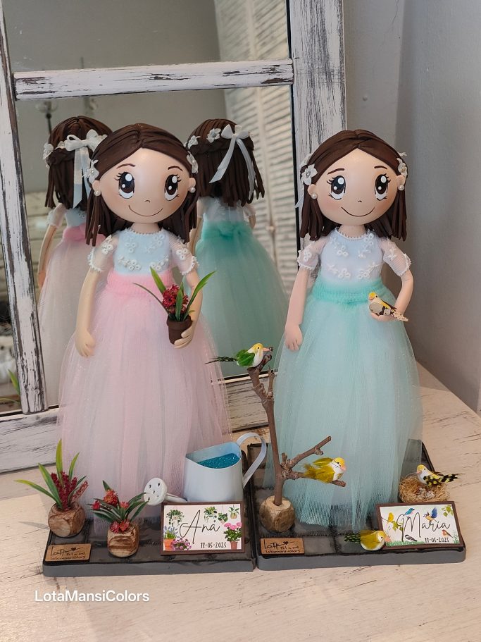 Dos muñecas con vestidos de tul, una rosa y otra verde, rodeadas de plantas con una regadera y de  pajaritos