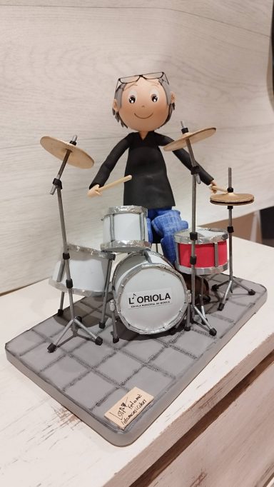 fofucha personalizada, vestida con jean casual camiseta negra sentado tocando la batería y los platillos 