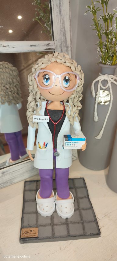 Fofucha personalizada de médico con cabello rizado,con un fonendo, con gafas  rosas y bata blanca, sosteniendo un medicamento.