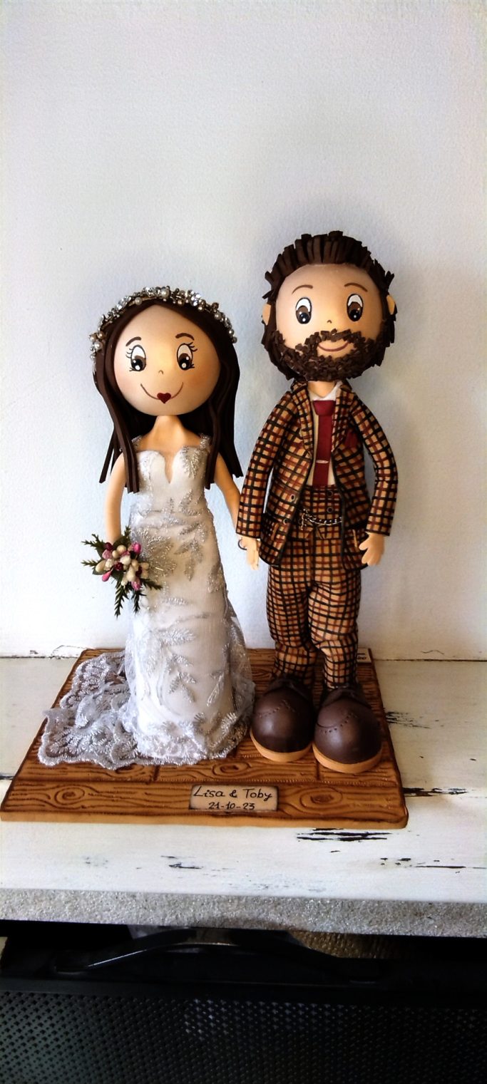 Pareja de novios de goma eva, ella con vestido blanco y él con traje marrón.