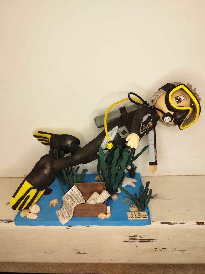 Muñeco de buzo con equipo de snorkel, rodeado de plantas marinas y un fondo azul.