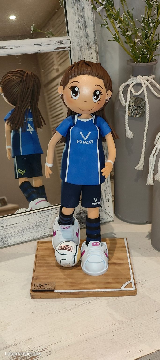 Muñeca con uniforme deportivo azul, deportivas blancas, con un balos a sus pies