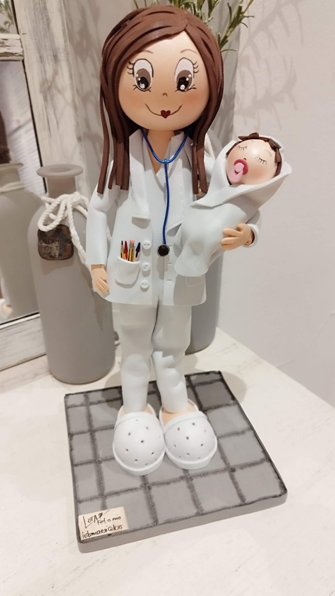 Fofucha doctora con un bebé en brazos, vestida de blanco y con estetoscopio.