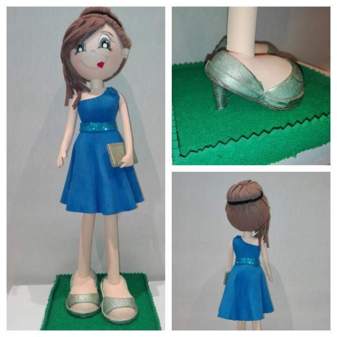 Muñeca con vestido azul con cinturón de purpurina y zapatos verdes, peinado con moño recogido.