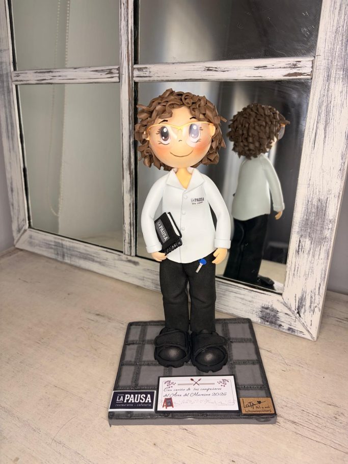 Muñeca con cabello rizado, sosteniendo un libro y una llave azul colgando del pantalón.