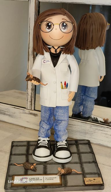 Fofucha personalizada, investigadora con gafas, bata blanca y jeans, sosteniendo unos ratoncitos en  la mano.