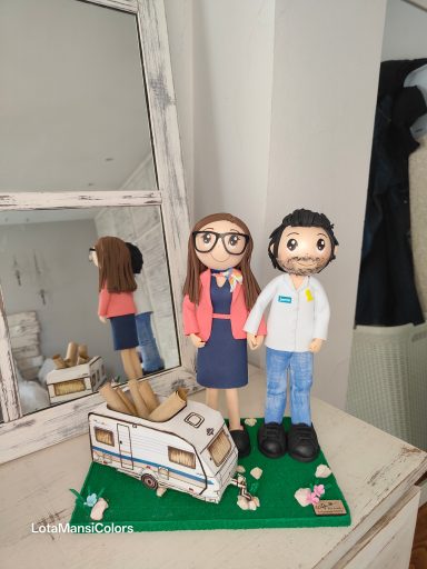 Figuras de pareja junto a una caravana en un entorno interior.