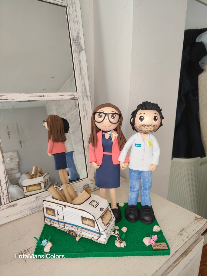 Figuras de pareja  junto a una caravana en un entorno interior.