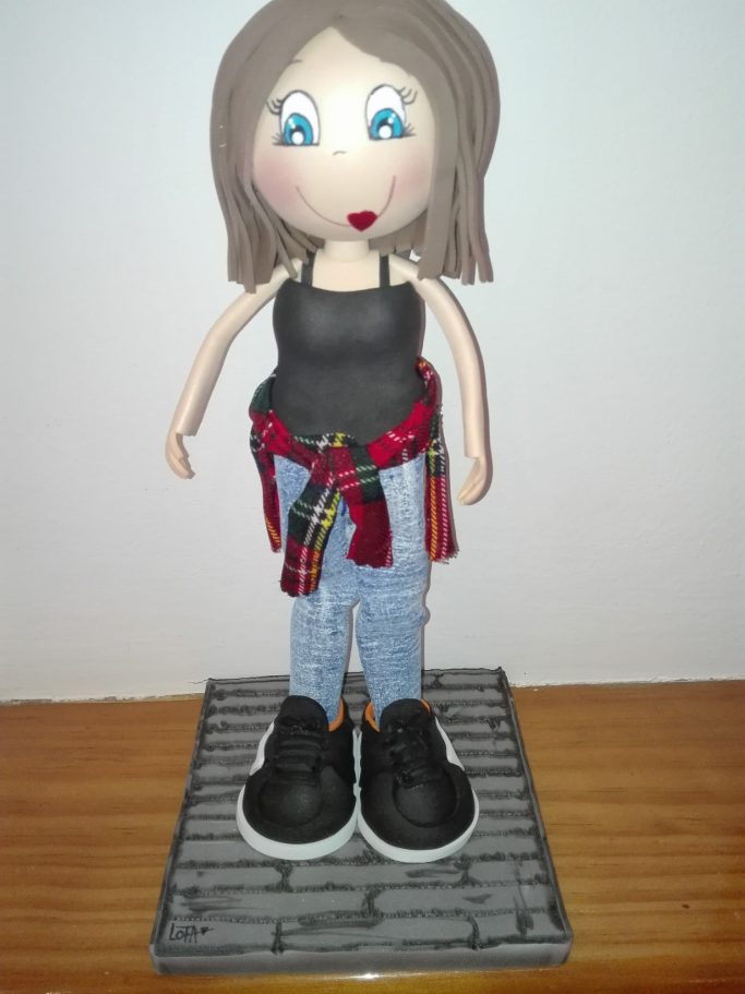 Muñeca  con cabello corto, camiseta negra y camisa de cuadros atada a la cintura, pantalones de mezclilla y zapatillas