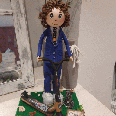 Muñeco con cabello rizado, vestido de traje azul y montado en un patinete. Decoraciones diversas