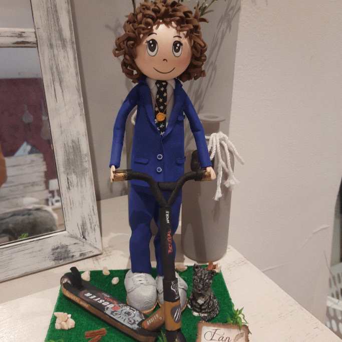 Muñeco con cabello rizado, vestido de traje azul y montado en un patinete. Decoraciones diversas