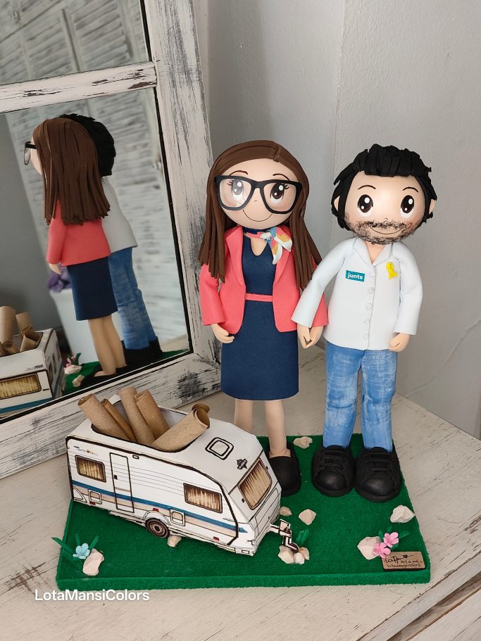 Muñeca mujer vestida de azafata y su marido vestido casual con una caravana de fondo y elementos decorativos.
