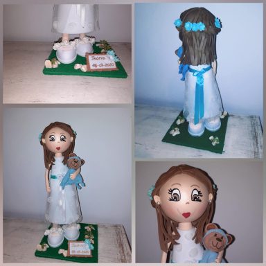 Muñeca de comunión con vestido blanco y osito de peluche, decorada con flores y cinturón azul.
