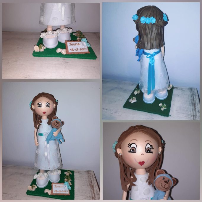 Muñeca de comunión con vestido blanco y osito de peluche, decorada con flores y cinturón azul.